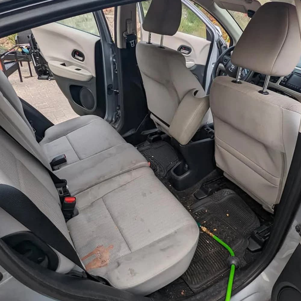 Rear seat before an interior deep clean, with a large stain and debris on the floor mats