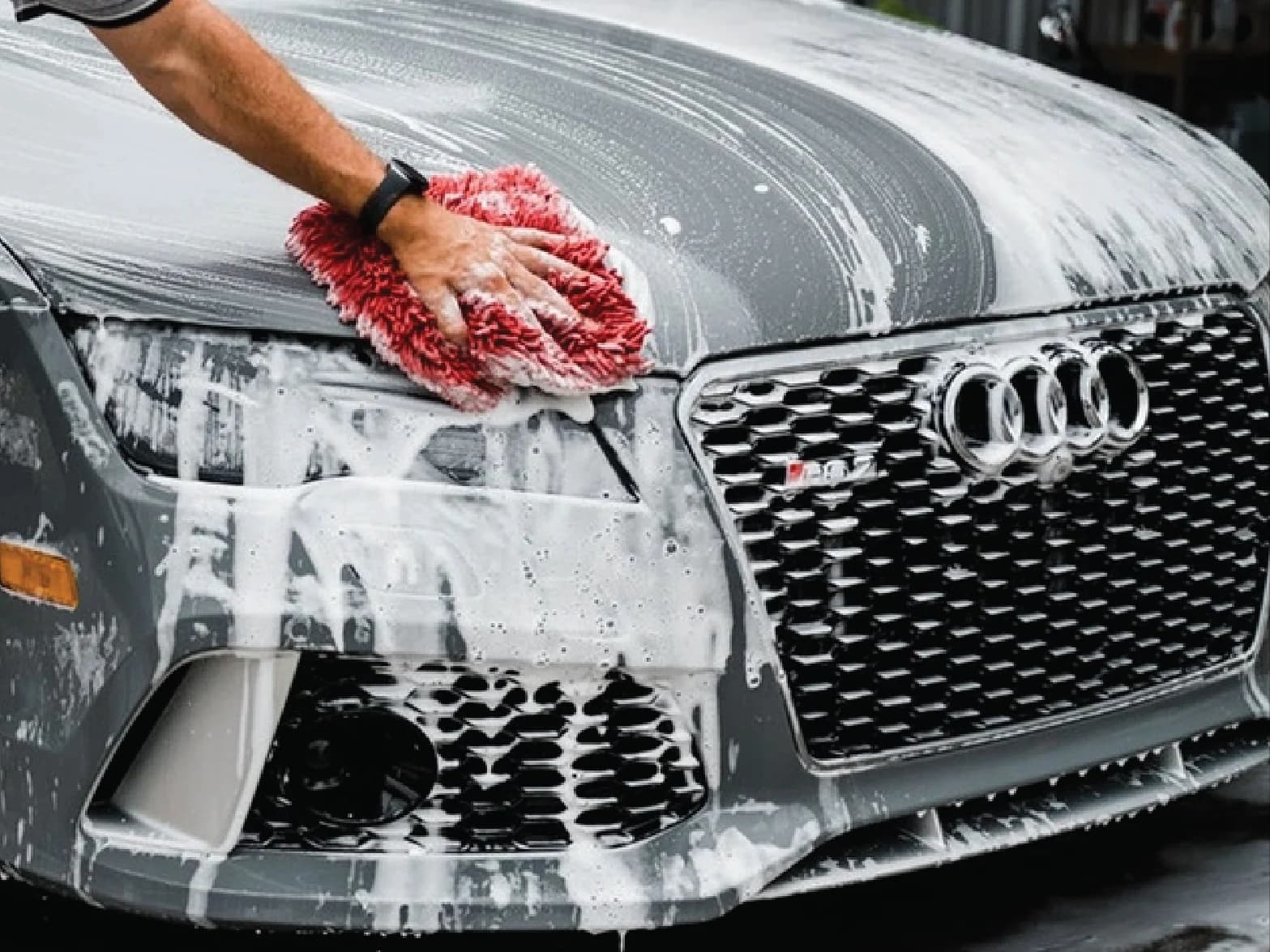 Detailer hand-washing a foam-covered gray Audi with a microfiber mitt