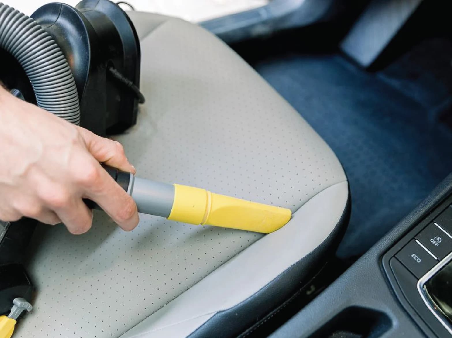 Detailer vacuuming a light gray perforated leather seat