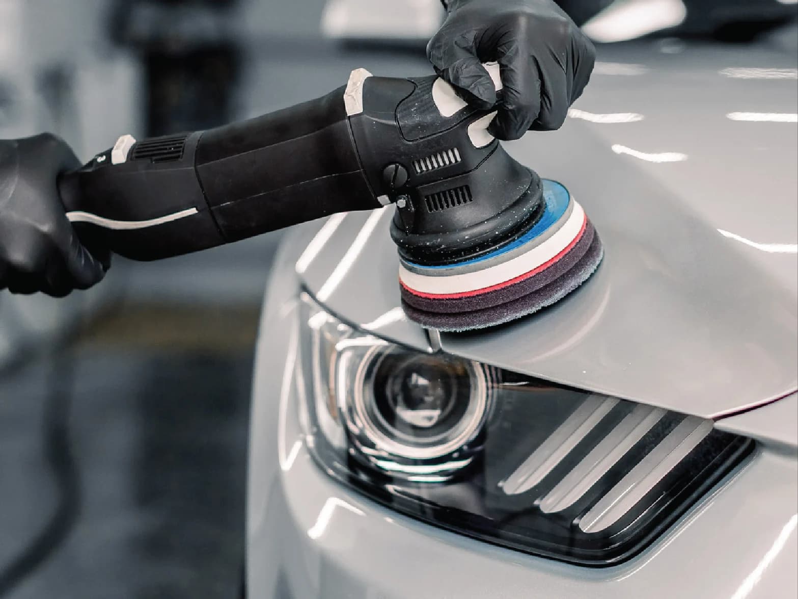 Dual-action polisher correcting the paint on a silver car's hood